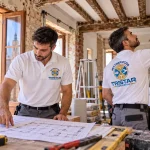 Operarios de Multiservicios Tristar Company con uniformes blancos y logo corporativo, rehabilitando una casa antigua en Zaragoza con paredes de ladrillo y vigas de madera.